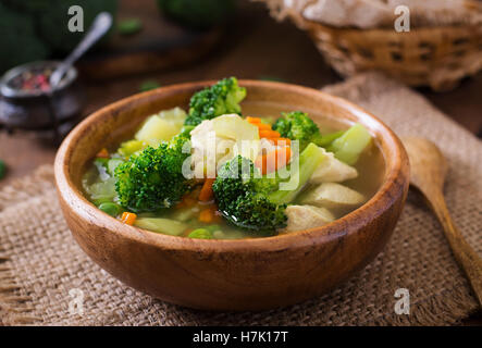 Hühnersuppe mit Brokkoli, grüne Erbsen, Möhren und Sellerie in Schüssel auf einem hölzernen Hintergrund im rustikalen Stil Stockfoto