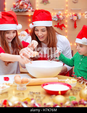 Glückliche Familie, die Vorbereitungen für Weihnachten, Mutter mit zwei niedlichen Kinder tragen rote Nikolausmütze, machen eine hausgemachte Kekse Stockfoto