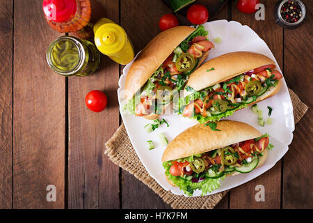 Hot Dog mit Jalapeno Paprika, Tomaten, Gurken und Salat auf hölzernen Hintergrund. Ansicht von oben Stockfoto