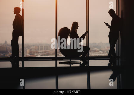 Silhouetten der Geschäft Leute zwei Mann und einer Frau ruht und warten auf das Treffen in der Nähe von großen Fenster in Luxusbüro Stockfoto