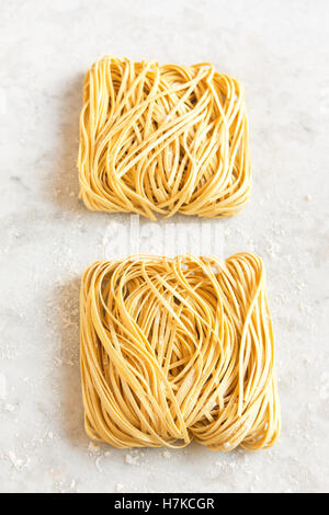 Rohe hausgemachte italienische Teigwaren Tagliatelle (chinesische Eiernudeln) über rustikale weißen Stein Hintergrund mit Textfreiraum Stockfoto