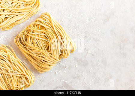 Rohe hausgemachte italienische Teigwaren Tagliatelle (chinesische Eiernudeln) über rustikale weißen Stein Hintergrund mit Textfreiraum Stockfoto