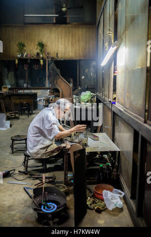 Ein Alter Mann Löten einige Sachen im Ladengeschäft Bangkok Stockfoto