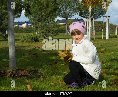 kleines Mädchen auf der Wiese im Herbst sammelt Blätter Stockfoto