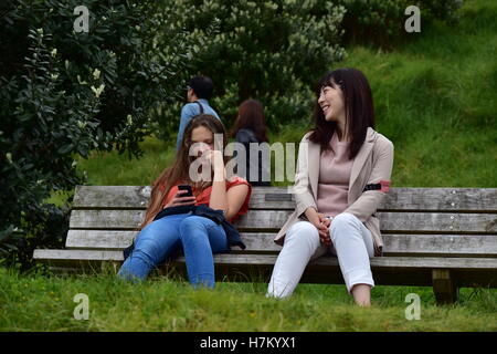 Japanische und europäische Mädchen sitzen auf der Parkbank. Stockfoto