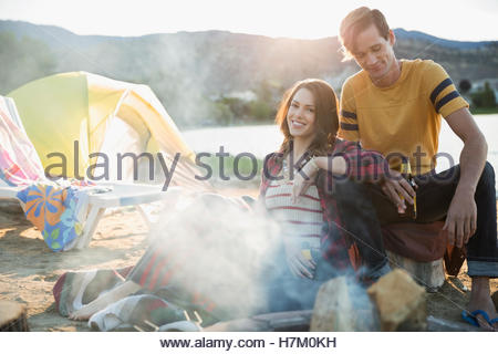 Junges Paar, entspannend und trinken Bier am Lagerfeuer am Seeufer Sommerstrand