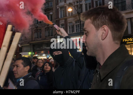 London, UK. 5. November 2016. Eine Figur in Schwarz trägt eine roten Rauch Fackel zum Protest durch Reiniger Union Vereinigten Stimmen der Welt und Unterstützern außerhalb John Lewis in der Oxford Street zu verlangen, dass das Unternehmen seine Reiniger fair behandeln auf der gleichen Grundlage wie andere Mitarbeiter, die dort arbeiten. John Lewis ist stolz auf seine "Partnerschaft"-Modell, unter denen diejenigen, die Arbeit in ihren Läden bekommen einen Teil ihrer Gewinne, sondern die Menschen, die die Geschäfte sauber zu halten als Bürger zweiter Klasse behandelt werden, von der jährlichen "Bonus" mit Löhnen nur ein paar Cent über dem nationalen Minimum an £7 ausgeschlossen. © Peter Marshall/Ala Stockfoto