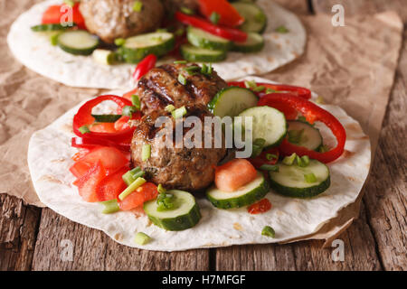 Gegrillte Frikadellen mit frischem Gemüse auf ein flaches Brot hautnah auf dem Tisch. horizontale Stockfoto