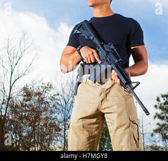 Mann mit Bäumen hinter einer AR-15 mit einer Pistole auf seiner Seite Stockfoto