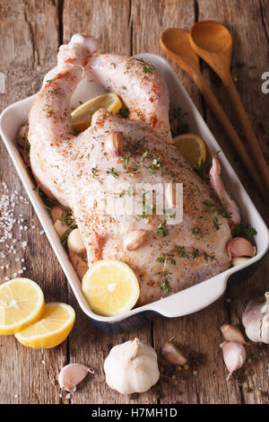 Rohe ganze Hähnchen mariniert mit Knoblauch, Thymian und Zitrone Nahaufnahme auf dem Tisch. Vertikal Stockfoto