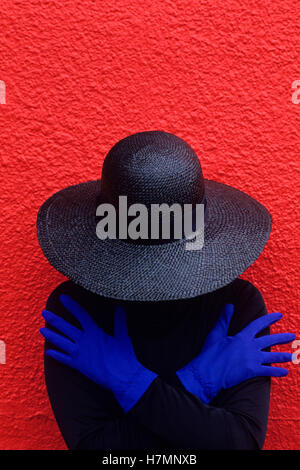 Frau vor einer roten Wand mit blauen Handschuhen bekleidet mit schwarzen Klamotten Seattle Washington State USA Stockfoto