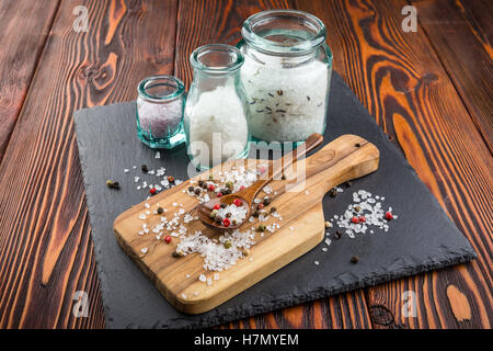 Salz in Gläsern, bestreut mit Salz und Pfeffer, Oliven Holz Löffel auf Schneidebrett Stockfoto