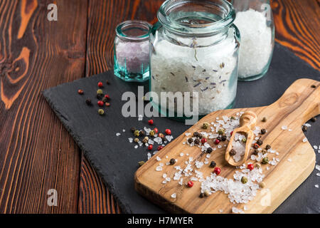 Salz in Gläsern, bestreut mit Salz und Pfeffer, Oliven Holz Löffel auf Schneidebrett Stockfoto