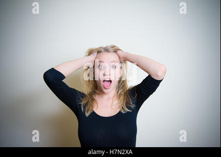 Junge, blonde Frau, schwarzes Hemd, erstaunt Weinen mit offenem Mund, Blick in die Kamera auf weißem Hintergrund Stockfoto