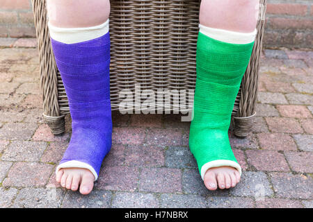 Teenager mit zwei farbigen Gips Beine draußen sitzen Stockfoto