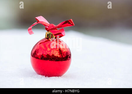 Eine glänzende rote Weihnachtskugel mit Bogen draußen im Winterschnee Stockfoto