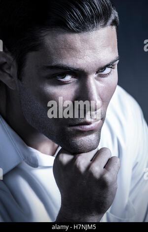 Hübscher junger Mann mit dunklen Bart-Stoppeln und modernen Frisur in schweren Kopf und Schultern Studioportrait mit kalte Töne. Stockfoto