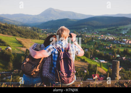 Reisen paar sitzen auf Holzbank mit Blick auf die Berge und Blick durch das Fernglas Stockfoto