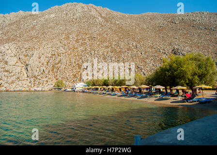 Strand von Saint Nicholas Bay auf Symi mit Sonnenschirmen und Liegestühlen Stockfoto