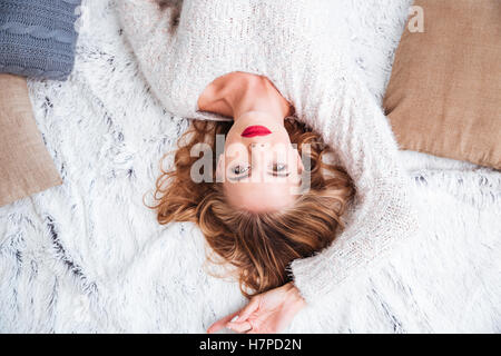 Draufsicht auf eine schöne junge Frau trägt roten Lippenstift und Pullover auf dem Teppich liegend Stockfoto