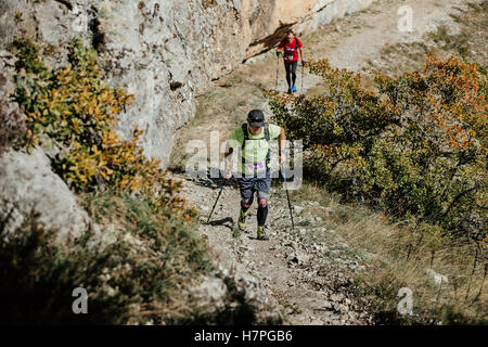 zwei männliche Athlet mit walking-Stöcken zu Fuß bergauf auf Hintergrund Klippe während Crimea Bergmarathon Stockfoto