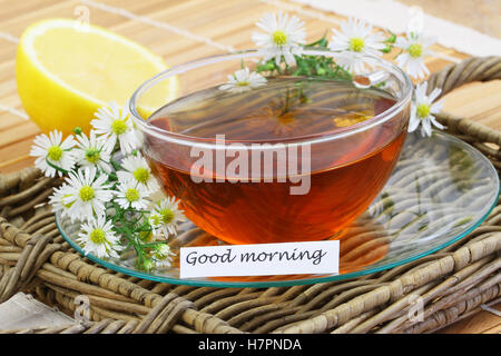 Guten Morgen Karte mit Tasse Kamillentee mit Kamillenblüten und frischer Zitrone Stockfoto