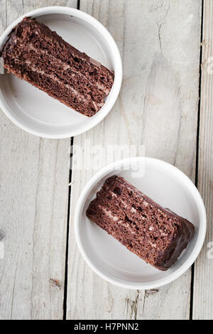 Zwei Stücke von Schokolade Torte mit Schokocreme und Glasur auf einem weißen Teller. Hölzerne Hintergrund. Ansicht von oben Stockfoto