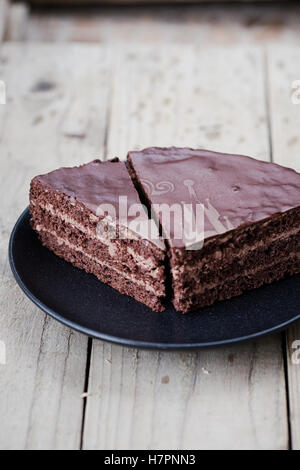 Stück Schokolade Dreischicht Kuchen mit Schokoladencreme und Glasur auf einem dunklen Teller. Hölzerne Hintergrund Stockfoto