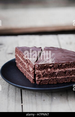 Schneiden von Schokolade Torte mit Schokocreme und Glasur auf einem dunklen Teller. Hölzerne Hintergrund Stockfoto