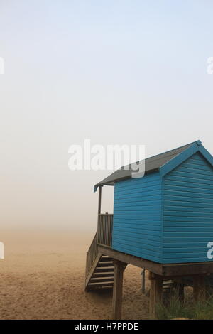 Blaue Strandhütte mit Blick auf einen nebligen Sandstrand am Brunnen Stockfoto