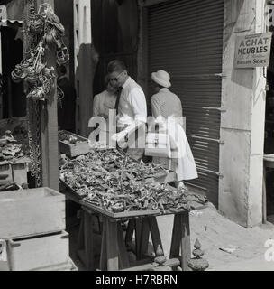 der 1950er Jahre, historisch, Blick romantisch zu zweit in Paris, Frankreich, auf ein großes Display von Sammlerstücke für den Verkauf auf einen Stand auf einer der vielen Flohmärkte der Stadt berühmt ist. Stockfoto