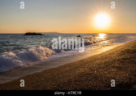 Kiesstrand mit Wellen im warmen Sonnenuntergang Stockfoto