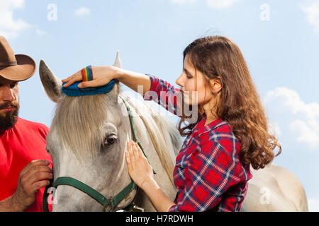 Junge Frau, die ihr schönes weißes Pferd Bürsten Stockfoto