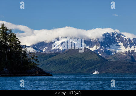Ein kleines Passagierboot, das an Einem sonnigen Tag durch den Passage-Kanal boomt, bewaldete Hügel und schneebedeckte Berge im Hintergrund, Prinz William... Stockfoto