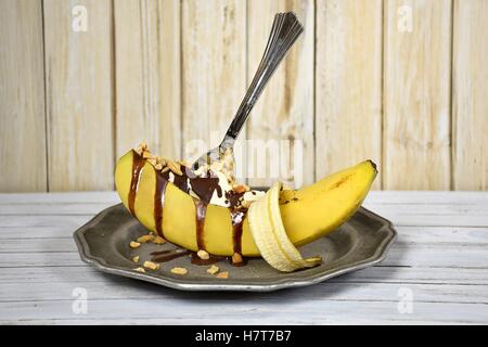 Bananensplit-Eisbecher mit Schokolade und Cashew-Nüssen in geschälte Banane auf Zinnteller tropft Stockfoto