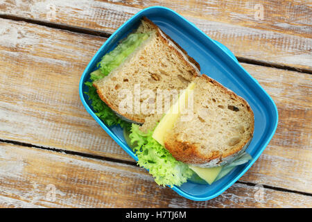 Lunch-Box mit Bauernbrot Brötchen mit Käse und Salat auf Holzuntergrund Stockfoto