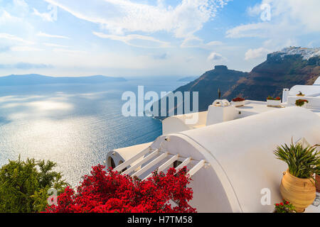 Ein Blick auf Caldera und Meer vom Hausdach verziert mit roten Flowerrs im Dorf Firostefani, Santorin, Griechenland Stockfoto