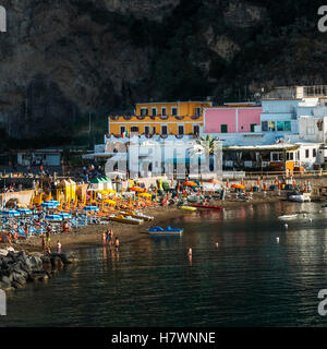 Farbenfrohen Gebäuden und Sonnenschirmen, Stühlen und Boote am Strand mit Schwimmer im Wasser; Sant Angelo, Ischia, Kampanien, Italien Stockfoto