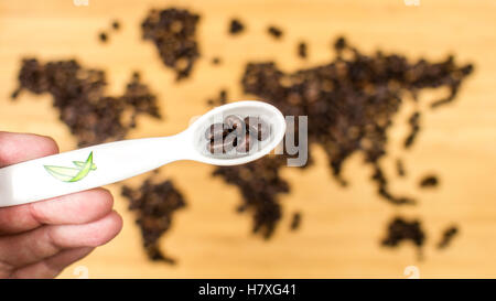 Mann hält einen weiße Keramik Löffel voller Kaffeebohnen mit Karte der Welt von gerösteten Arabica Kaffeebohnen Stockfoto