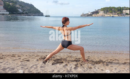 Eine Frau Yoga am Strand in Mallorca. warrior Pose dargestellt. Stockfoto