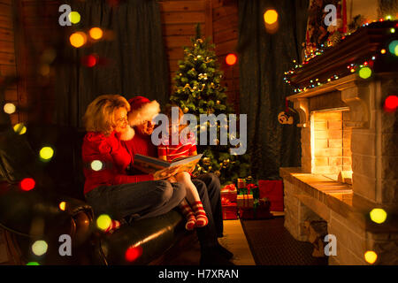 Familie Buch auf Sofa vor Kamin innen Weihnachten eingerichtetes Haus Stockfoto