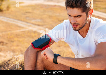 Konzentrierte sich junge Sportler sitzen und mit smart-Uhr im freien Stockfoto