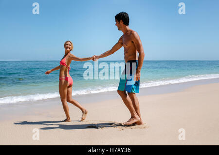 Voller Länge Schuss von romantisch zu zweit zu Fuß auf schönen tropischen Strand. Glücklicher junger Mann und Frau geht ins Meer, mit woma Stockfoto