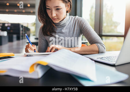 Schließen Sie herauf Bild an einer jungen Studentin tun Aufgaben in Bibliothek. Asiatische Frau Notizen aus Lehrbuch. Stockfoto