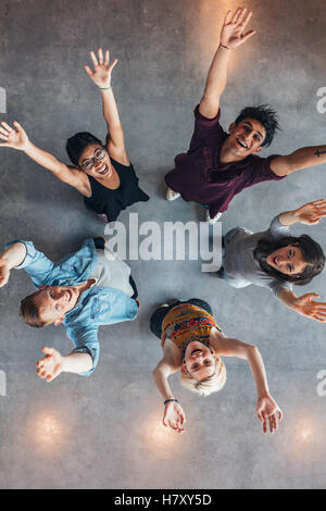 Blick von oben auf junge Menschen, die zusammen stehen und mit erhobenen Armen in die Kamera blicken. universitätsstudenten jubeln. Stockfoto