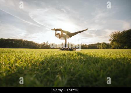 Passen Sie junges Paar beim Acro Yoga. Mann auf dem Rasen liegen und Frau in seinen Füßen balancieren. Akrobatische Balance im Park. Stockfoto