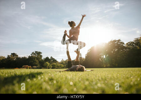 Gesunde junge Paar Acro Yoga auf dem Rasen zu tun. Mann und Frau verschiedene Yogastellungen paarweise im Freien im Park zu tun. Stockfoto