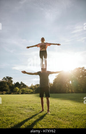Starke junge paar akrobatische Yoga machen Übung im Park. Frau stehend auf den Schultern des Mannes und Ausgleich mit Armen abhebe Stockfoto