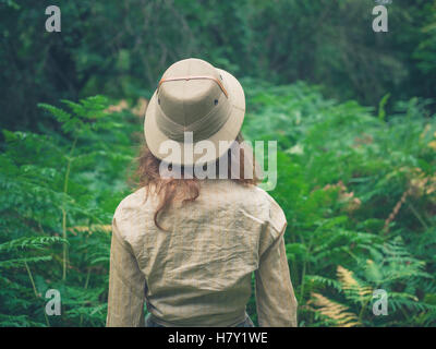 Eine junge Frau mit einem Safari-Hut ist einen Wald mit vielen grünen Farnen erkunden Stockfoto