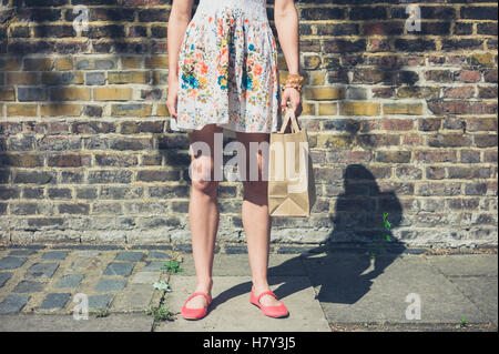 Eine junge Frau trägt ein Sommerkleid steht auf der Straße mit einer Papiertüte Stockfoto